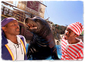 A sea lion interacts with two costumed trainers during a show.
