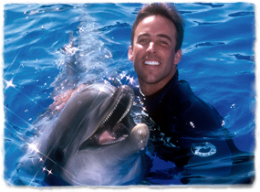 A trainer pets a dolphin while the two pose in the water.