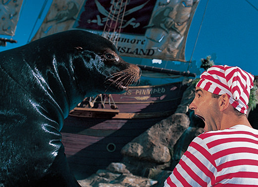 A costumed trainer makes a comedic exaggerated gasp expression while face-to-face with a sea lion