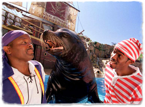 A sea lion interacts with two costumed trainers during a show.